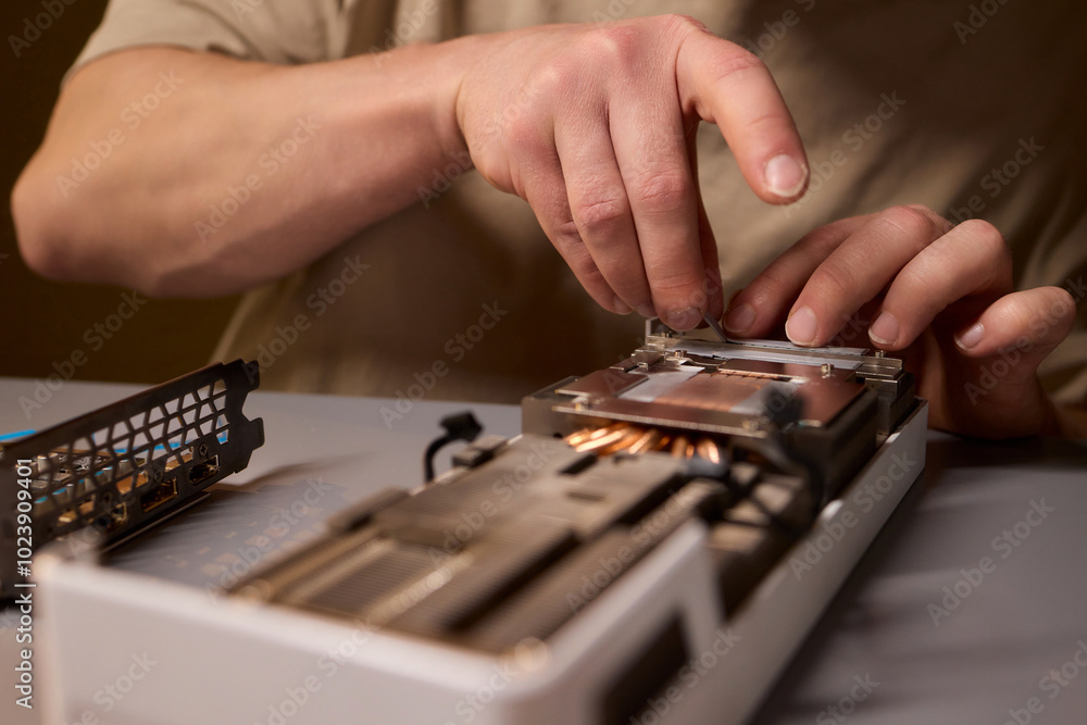 Poster hand repairing a graphics card through the application of thermal paste for better performance