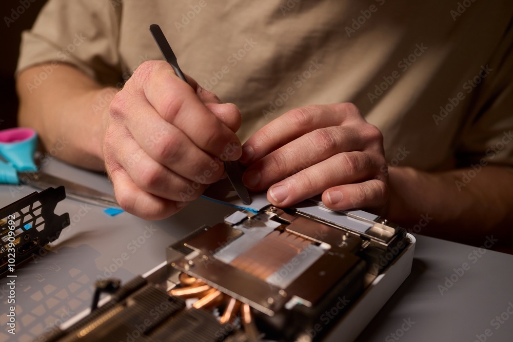 Poster hand repairing a graphics card through the application of thermal paste for better performance