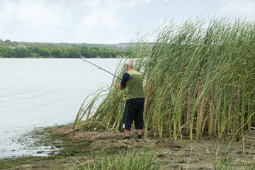 Fisherman with rod fishing near lake at summer