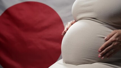 Unrecognizable future mother expecting baby on japanese national flag background. Pregnant woman touching belly. Demography crisis, population problems in Japan. - Powered by Adobe