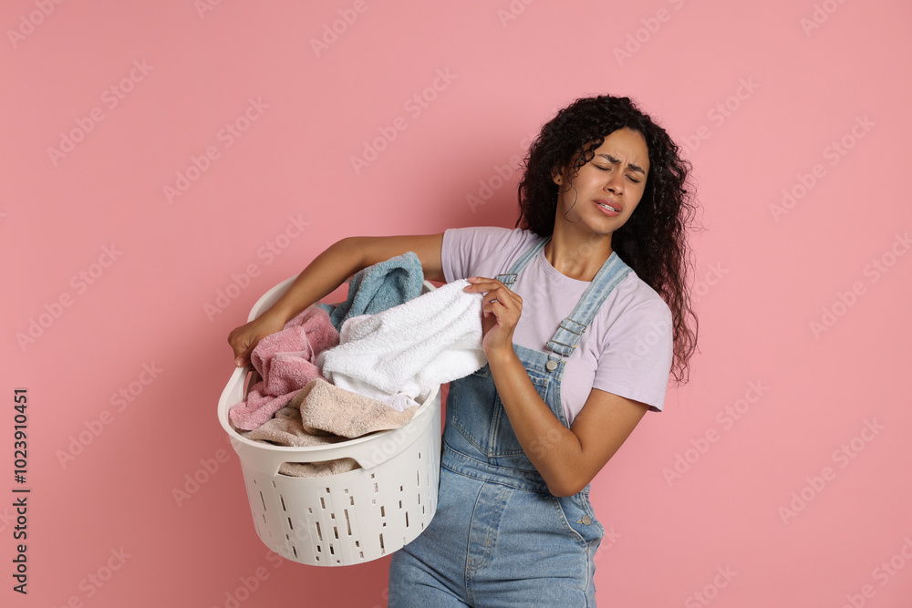 Wall mural Displeased woman with basket full of laundry on pink background