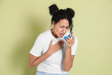 Young woman using asthma inhaler on light green background