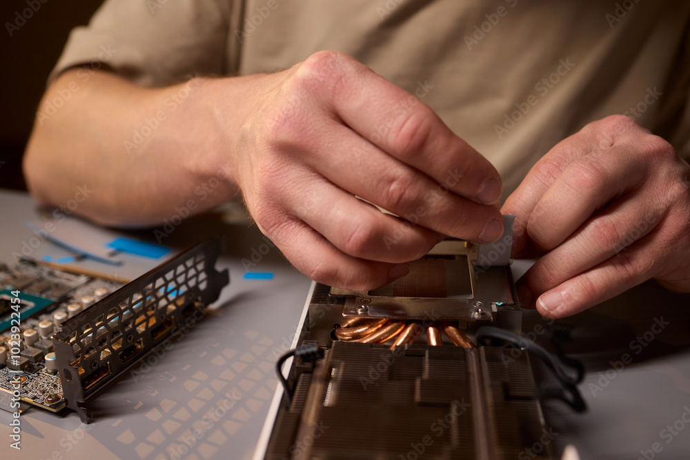 Poster hand repairing a graphics card through the application of thermal paste for better performance