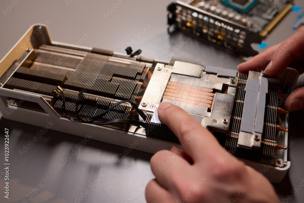 Poster hand repairing a graphics card through the application of thermal paste for better performance