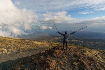Hiking person looking at view of volcanic landscape of Mount Etna with black lava and yellow grass...