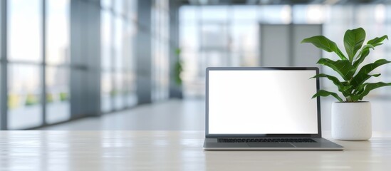 A modern laptop with a blank screen is placed on a table in front of an office window, overlooking the outside landscape