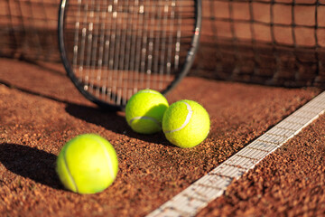 Tennis ball with rocket near grid at outdoor summer sunny court closeup