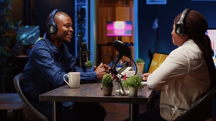 African american influencer recording podcast with guest, using professional equipment in home studio. Joyful host discussing with woman live during broadcasting session for internet show
