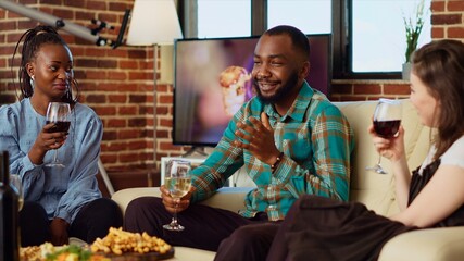 African american man telling enthralling story to BIPOC apartment party guests during weekend...