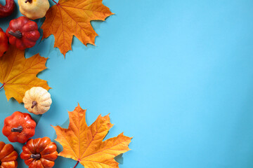 Autumn flat lay with decorative pumpkins and orange maple leaves on a blue background. Flat lay, top view, copy space.