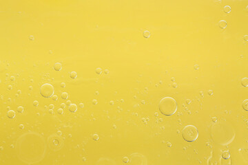 Essential oil bubbles on yellow background, macro view. Cosmetic product
