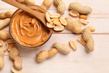 Tasty peanut butter in bowl and nuts on wooden table, flat lay