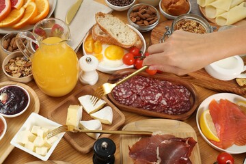 Woman eating different food during brunch at wooden table, closeup