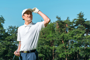 新緑の中でゴルフウェアを着た男性ゴルファー（ゴルフコース・アカデミー・会員権）
