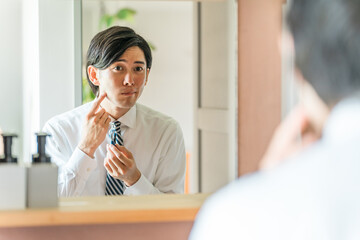 朝出勤前に洗面所で髭剃りをするスーツ姿の若いアジア人ビジネスマン
