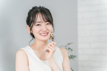 美顔器でマッサージするルームウェア姿の若いアジア人女性
