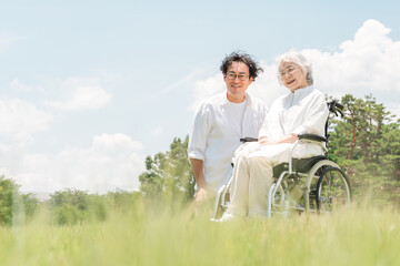 公園にいる車椅子に乗ったシニア女性と介助する男性（介護・親子・老人ホーム）
