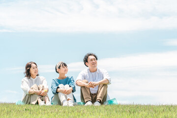 青空の見える公園・丘に座る家族・親子（父親・母親・娘）
