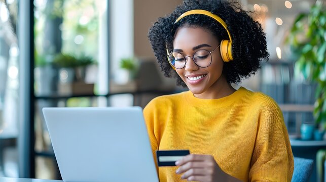 African American woman using a laptop for online shopping credit card in hand enjoying discounts and sales while wearing headphones in a digital tone with an analogous color scheme