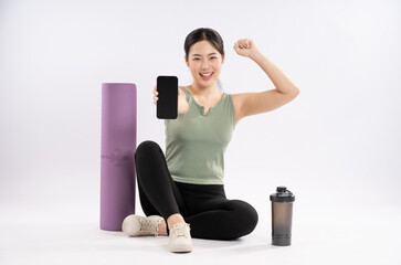 Full body image of young Asian girl wearing sports clothes and using phone , posing on white background