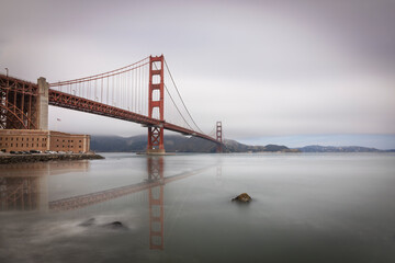 A serene view of the iconic Golden Gate Bridge shrouded in mist, reflecting gracefully over tranquil waters.