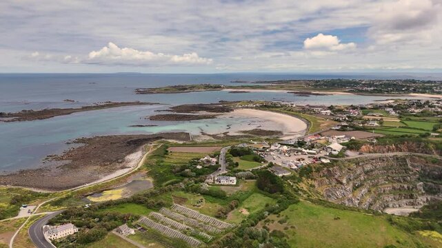 Guernsey.High drone flight over fields,derelict greenhouses, Les Vardes Quarry and golden beaches on West Coast on bright day
