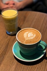A teal mug with intricate Rosetta latte art on a wooden table in a cozy café. The natural light highlights the craftsmanship, offering a peaceful setting for a coffee lover's lunch break.
