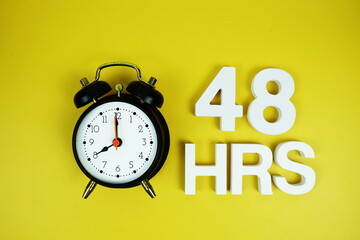 48 Hrs alphabet letters and alarm clock top view on yellow background