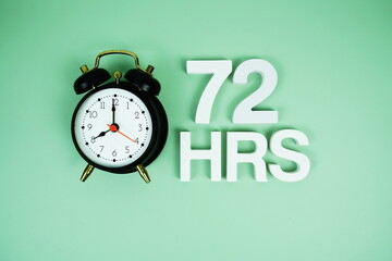 72 Hrs alphabet letters and alarm clock top view on green background