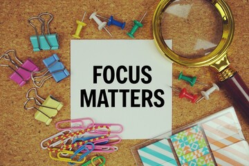 Focus Matters text on paper card with magnifying glass and stationery on cork board background