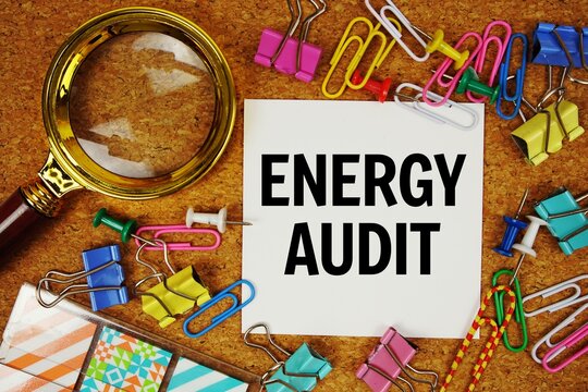 Energy Audit text on paper card with magnifying glass and stationery on cork board background