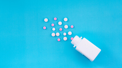 Flat lay of white bottle with white and pink medicine pills spread out on blue background. Concept of drugstore, pharmacy, healthcare, medicine, pharmaceutical business.