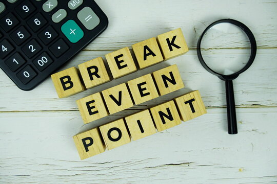 Break Even Point with wooden blocks alphabet letters and magnifying glass, calculator top view on wooden background