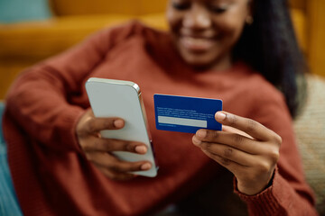 Close up of black woman using credit card and cell phone while ordering on the internet.