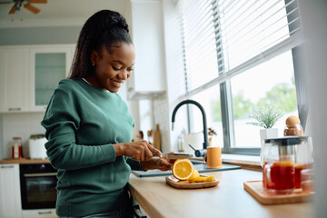 Happy black woman slicing lemon while making tea at home.