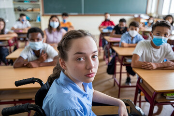 Caucasian schoolgirl in a wheelchair with diverse classmates in a school classroom, highlighting education and inclusivity
