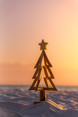 Rustic timber Christmas Tree with star on beach sand with golden hour morning light