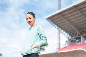 Asian woman wearing blue sportswear Stand and put both hands in your pockets. outdoor exercise Exercise in the stadium She is exercising and holding a water bottle. active living