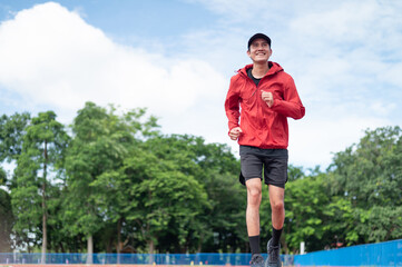 Obraz premium Happy asian man in red sport suit with cap jogging at stadium morning exercise Asian young man exercising on a treadmill outdoor exercise Professional athletes, exercising or playing sports