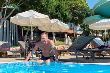 A middle-aged European man has moved himself from his wheelchair to the edge of a pool and is about to swim