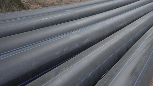 Long plastic black pipes of large diameter lie on the street. Close-up. Sewer pipes, water pipes, heating pipes. High quality 4k footage