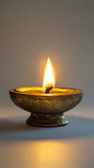 A close-up of a traditional brass oil lamp with a bright flame, set against a simple gray background.