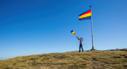 Person waving blue, yellow, and red flag on grassy hill under clear sky