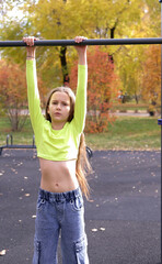 Girl doing exercises on horizontal bar outdoors during training, practicing pull-ups on horizontal...