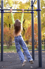 Girl doing exercises on horizontal bar outdoors during training, practicing pull-ups on horizontal...