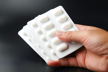 hand holding pills Medicine tablet capsules in blister pack on a black background