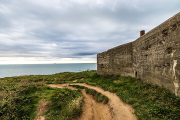Fototapeta premium A winding path runs along a coastal cliff with a vintage stone wall, guiding to a breathtaking ocean vista