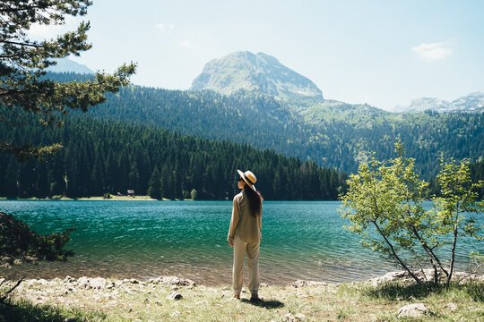 Woman stands by the water against the backdrop of forest and mountain