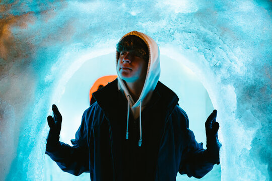 Teenage boy in coat stands in ice arch in ice cave