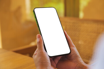 Mockup image of a woman holding and using mobile phone with blank desktop at home